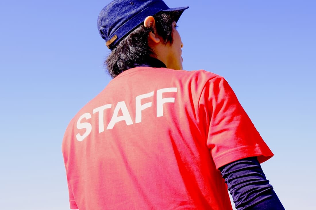 A staff member photographed from behind wearing a branded cap and staff shirt